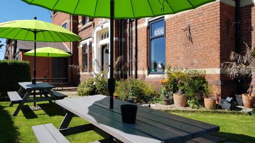 uma mesa de piquenique com dois guarda-chuvas verdes num quintal em The Mon Fort em Bridlington