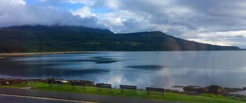 three benches sitting on the side of a lake at Hunters Guest House in Brodick