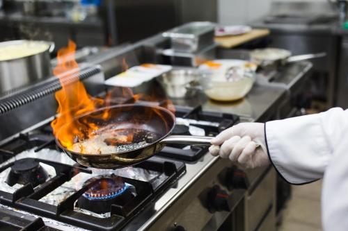 a person cooking food in a wok on a stove at Hotel Jelena in Banja Luka