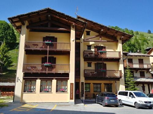un bâtiment avec balcon et voitures garées dans un parking dans l'établissement CHALET SEGGIOVIA, à Pontechianale