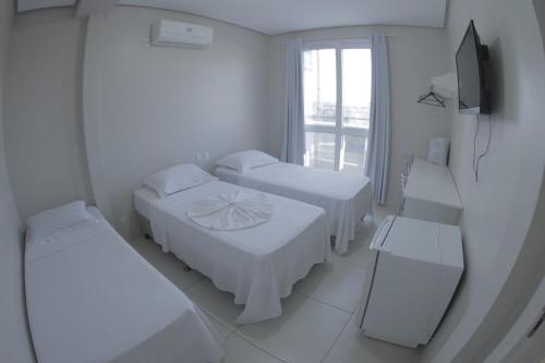 a white room with three beds and a television at Grande Hotel in Gurupi