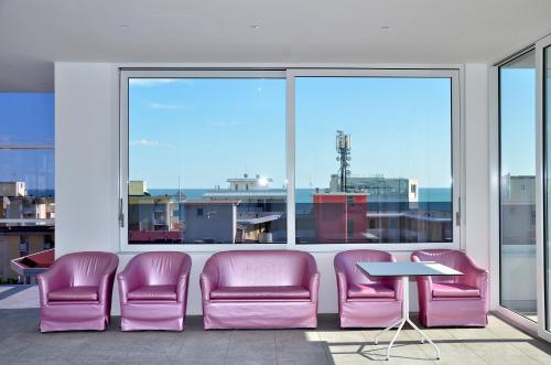 a waiting room with pink chairs and a table and windows at Hotel Amburgo in Bibione