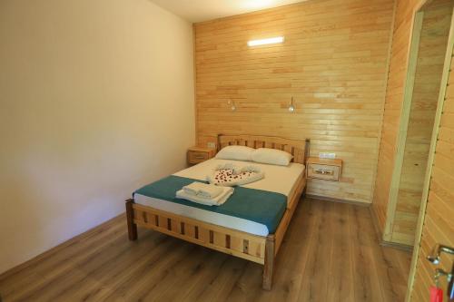 1 dormitorio con 1 cama y pared de madera en Tunays Pansiyon, en Cıralı