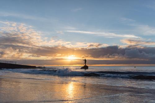 a person standing on a rock in the ocean at sunset at VISTA PLAYA Y MAR - sea view, wifi and AC in Melenara