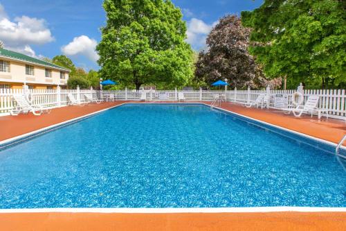 a large swimming pool with white chairs and trees at Baymont by Wyndham Harrisburg in Harrisburg