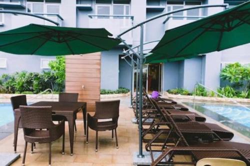 uma mesa e cadeiras com guarda-sóis verdes ao lado de uma piscina em Cubao ManhattanHeights Unit 11A Tower B, 2BR em Manila