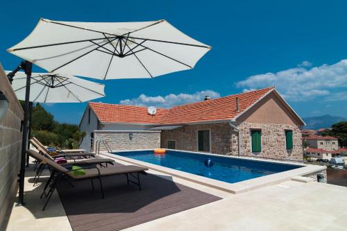 a swimming pool with an umbrella and chairs and a house at Apartments Ivana in Postira
