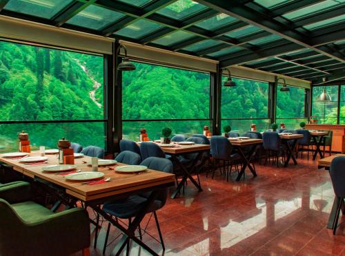 un restaurante con mesas, sillas y ventanas grandes en Ayder Villa de Pelit Hotel, en Ayder