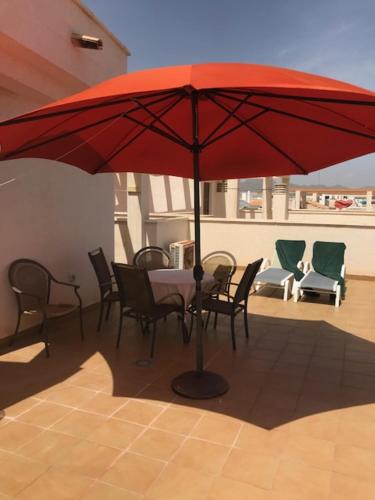 a red umbrella on a patio with chairs and a table at Apartamento La Marina - VVMU057 in Bolnuevo