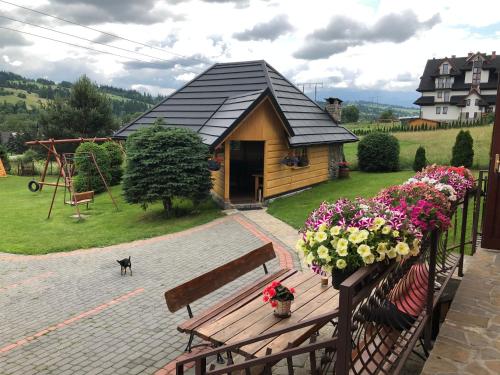 a wooden bench sitting in front of a house with flowers at Pokoje Gościnne Kornelia- Jacuzzi, sauna ! in Biały Dunajec