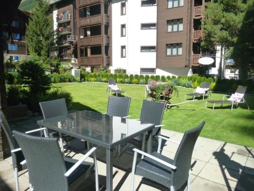 a patio with a table and chairs and a lawn at Jolimont Apartments in Zermatt