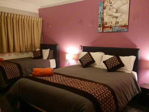 two beds in a room with pink walls at New Olympic Motel in Lismore