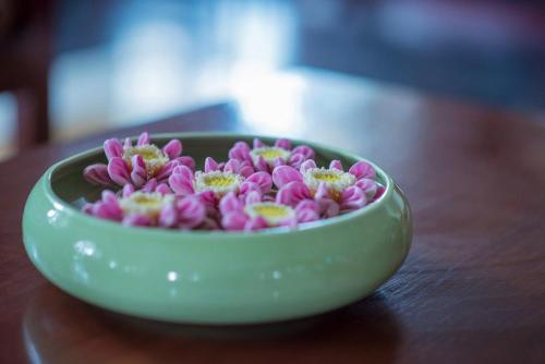 a green bowl filled with pink flowers on a table at Baitong Heritage Hotel in Siem Reap