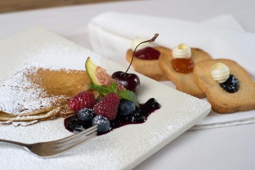a plate of pancakes with berries and jam and other desserts at Hotel Vedig in Santa Caterina Valfurva