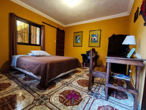 a bedroom with yellow walls and a bed and a table at Maison Bougainvillea in Antigua Guatemala
