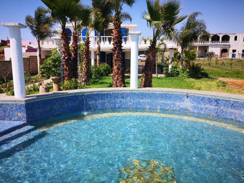 una piscina di fronte a una casa con palme di RIAD DES OISEAUX a El Aouamra