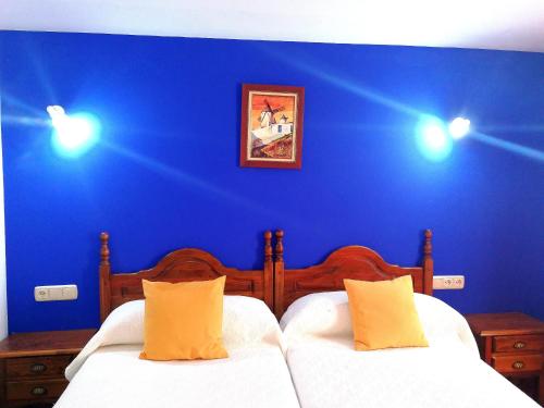 a bedroom with blue walls and two beds with yellow pillows at Hostal Restaurante Ego's in Campo de Criptana