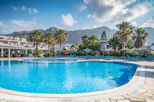 a large swimming pool with palm trees and mountains at Evripides Village in Kardamaina