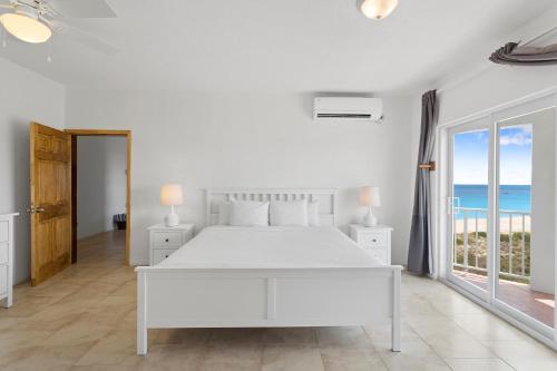 a white bedroom with a bed and a view of the ocean at Turtle's Nest Beach Resort in Meads Bay