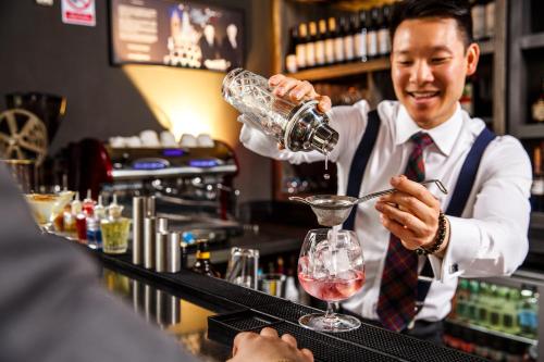 a man pouring a drink into a martini glass at a bar at ibis Styles London Ealing in London