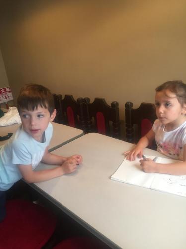 two young children sitting at a table writing on paper at Guest house daisho oshiro asobi in Matsue