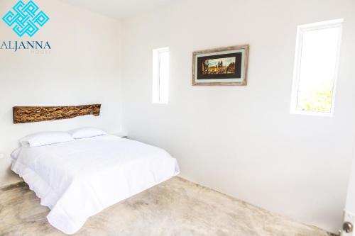 a white bedroom with a bed and two windows at Aljanna House in Bacalar