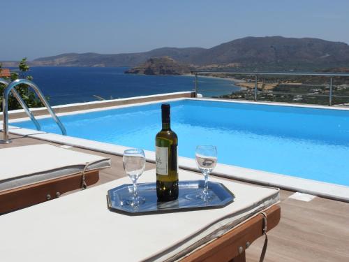 a bottle of wine and two glasses on a table near a swimming pool at Villa Aiolos in Palekastron
