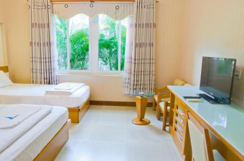 a room with two beds and a desk and a window at Mui Tau Hotel Phan Ri Cua in Tuy Phong