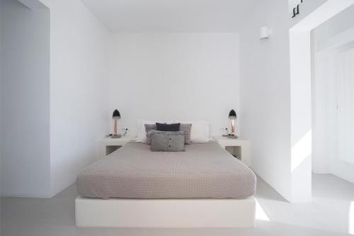 a white bedroom with a white bed with two lamps at Thiro Santorini in Fira