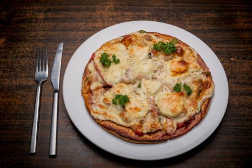 a pizza on a white plate next to a fork and knife at Baitong Heritage Hotel in Siem Reap