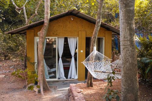 a small yellow cottage with a porch and two swings at Namaste Jungle - A Boutique Homestay in Assagao