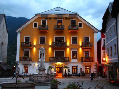 a large yellow building with a fountain in front of it at Seehotel Grüner Baum in Hallstatt