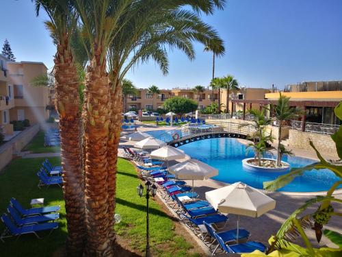 una piscina del complejo con sillas, sombrillas y palmeras en Pagona Holiday Apartments, en Pafos