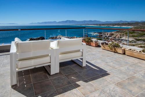 a balcony with white chairs and the ocean at Cliff Lodge in Gansbaai