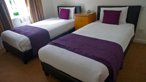 two beds in a hotel room with purple sheets at Abbey Court Hotel - Hyde Park in London