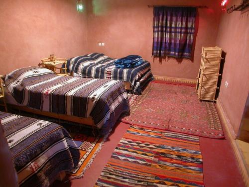 a room with three beds and a rug in a room at Maison d'Hôtes Agdal Telouet in Tiguidert