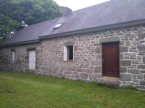a stone house with a wooden door and a yard at Le Botcol in Plouguernével
