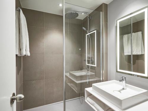a white bathroom with a sink and a shower at Novotel Ieper Centrum in Ypres