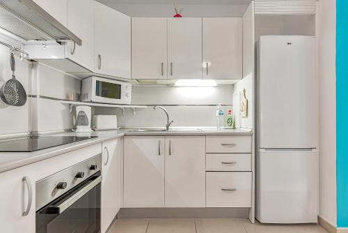 a white kitchen with white cabinets and a refrigerator at Apartamento en Alcalá, con aparcamento, con aircondicionador in Alcalá