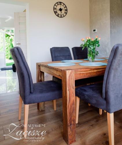 a dining room table with blue chairs and a clock on the wall at Apartament Zacisze in Uherce Mineralne