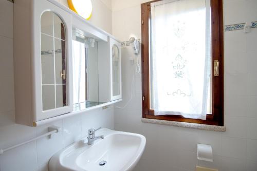 a white bathroom with a sink and a window at Rosa Holiday Home in Villasimius