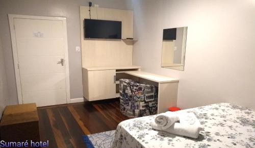 a small white room with a bed and a tv at Sumare Hotel in Florianópolis