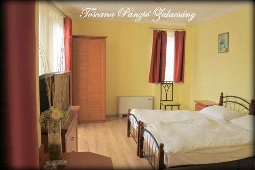 a bedroom with two beds and a table and a window at Toscana Panzió in Zalacsány