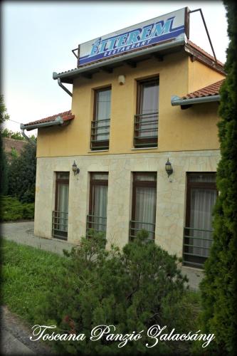 a yellow building with a sign on top of it at Toscana Panzió in Zalacsány