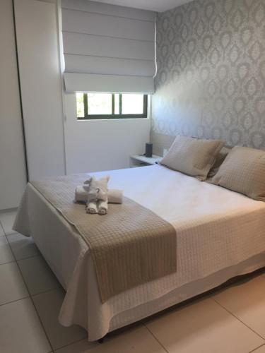 een slaapkamer met een groot wit bed met een knuffeldier erop bij Apto Luxo Iloa Barra de São Miguel in Barra de São Miguel