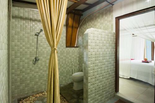 a bathroom with a shower with a toilet and a mirror at Ina Gili Guesthouse in Gili Air