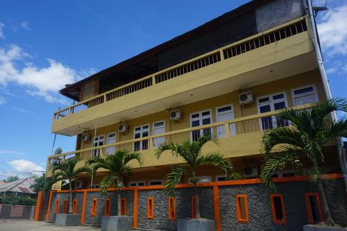 a yellow building with palm trees in front of it at Orange Hotel in Labuan Bajo