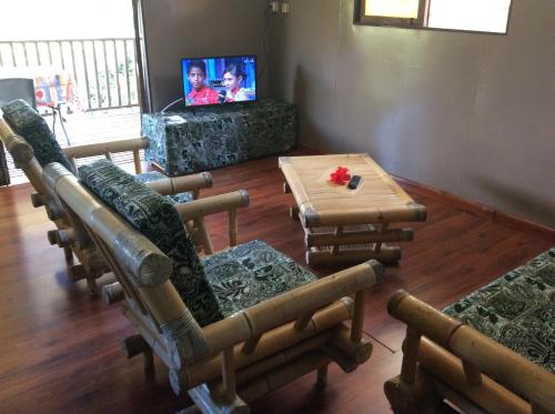 ein Wohnzimmer mit Stühlen, einem Tisch und einem TV in der Unterkunft Simplicité Marquises in Atuona