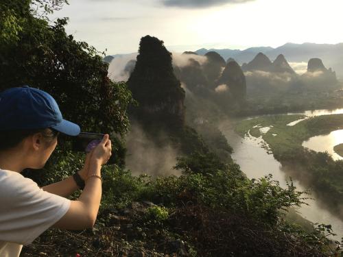 a person taking a picture of a river and mountains at Yangshuo Yunshe Mountain Guesthouse in Yangshuo
