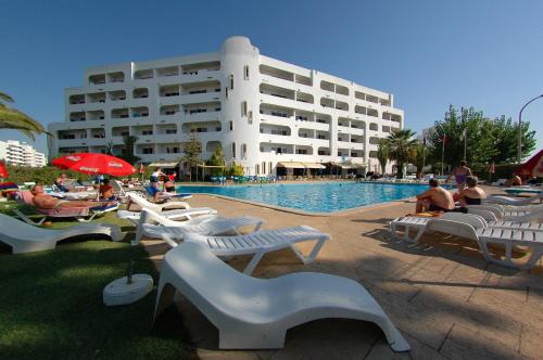 a large building with a pool with people sitting around it at Apartamentos Turisticos Silchoro in Albufeira